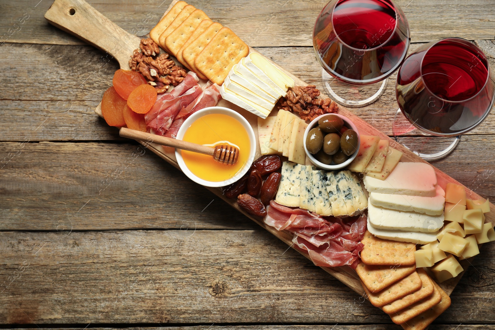 Photo of Different types of delicious cheese, other snacks and wine on wooden table, flat lay. Space for text