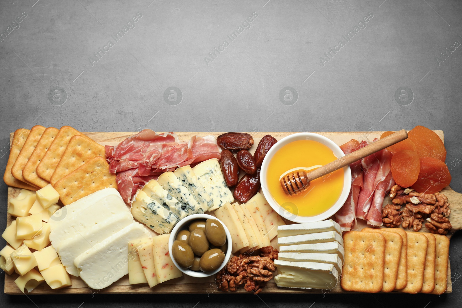 Photo of Different types of delicious cheese and other snacks on grey table, top view. Space for text