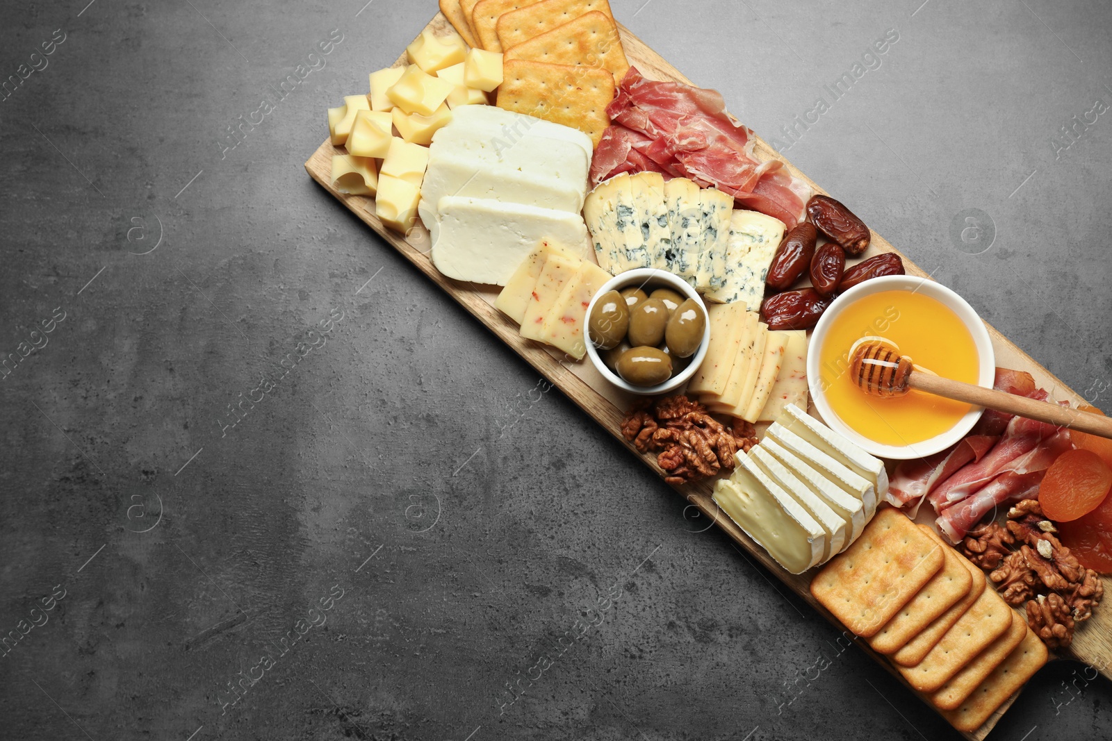 Photo of Different types of delicious cheese and other snacks on grey table, top view. Space for text