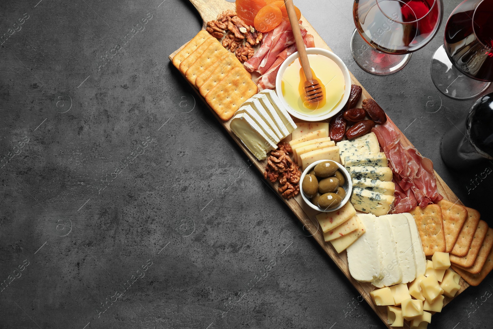 Photo of Different types of delicious cheese, other snacks and wine on grey table, flat lay. Space for text