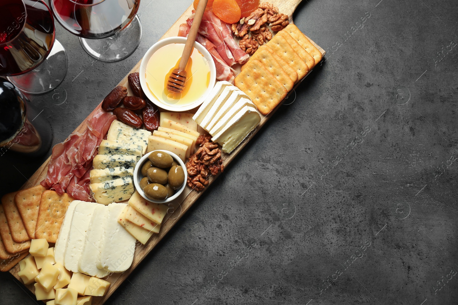 Photo of Different types of delicious cheese, other snacks and wine on grey table, flat lay. Space for text