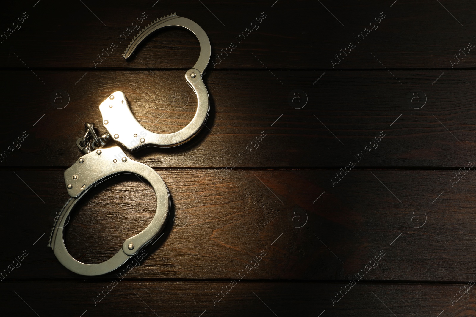 Photo of Metal chain handcuffs on wooden table, top view. Space for text