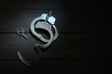 Photo of Metal chain handcuffs and key on black wooden table, top view. Space for text