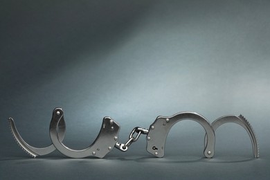 Photo of Metal chain handcuffs on grey background, closeup. Space for text