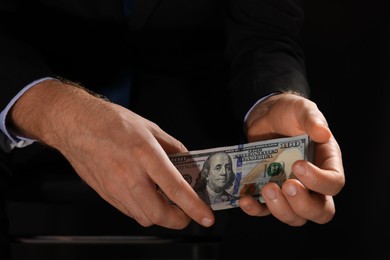 Photo of Corruption concept. Man holding dollar banknotes on black background, closeup