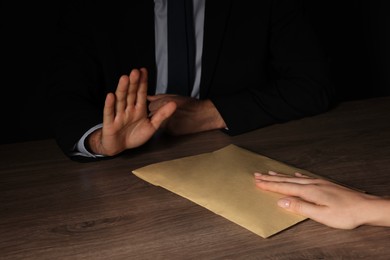 Photo of Corruption concept. Woman giving envelope with money to man at wooden table, closeup