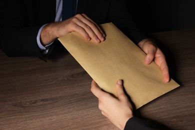 Photo of Corruption concept. Woman giving envelope with money to man at wooden table, closeup