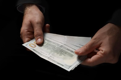 Photo of Corruption concept. Man holding dollar banknotes on black background, closeup