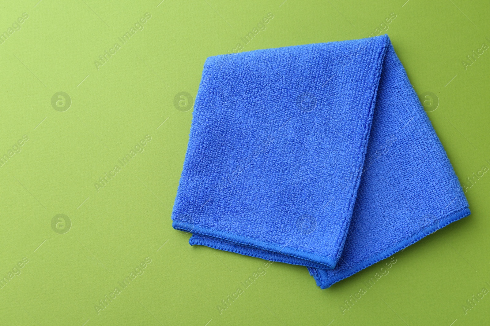 Photo of Clean blue microfiber cloth on green background, top view. Space for text