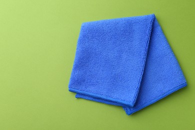 Photo of Clean blue microfiber cloth on green background, top view. Space for text