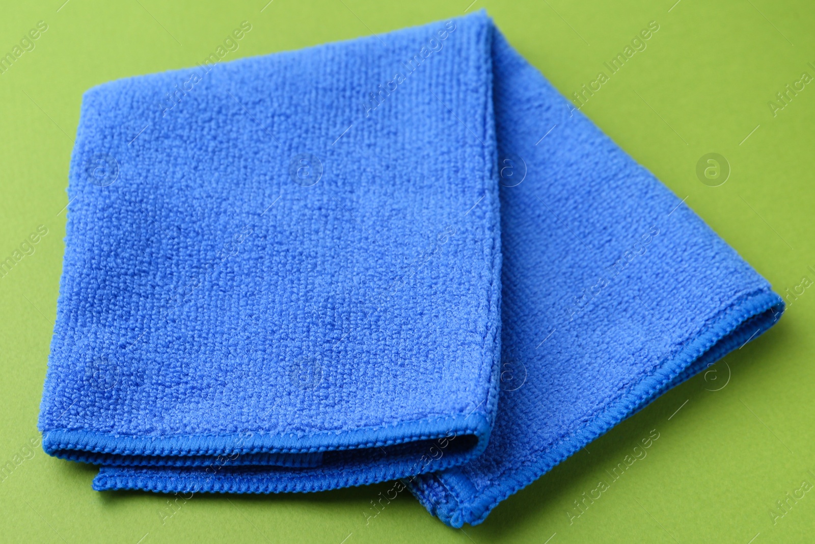 Photo of Clean blue microfiber cloth on green background, closeup