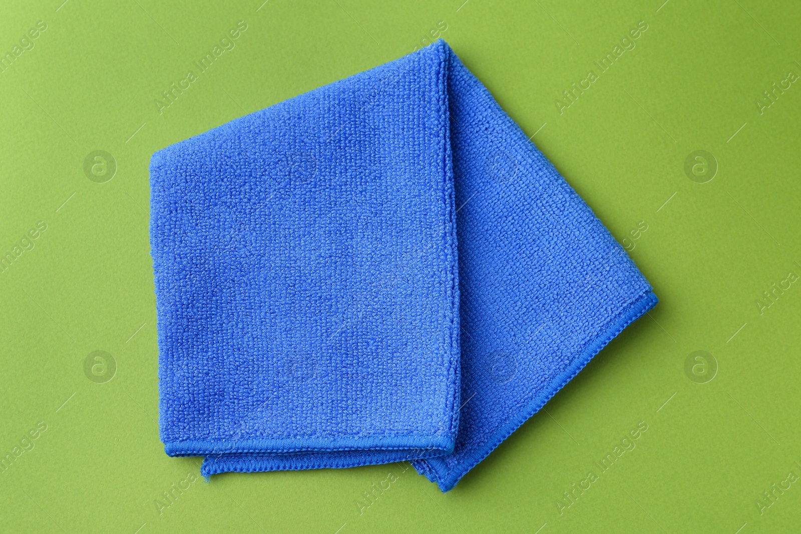 Photo of Clean blue microfiber cloth on green background, top view