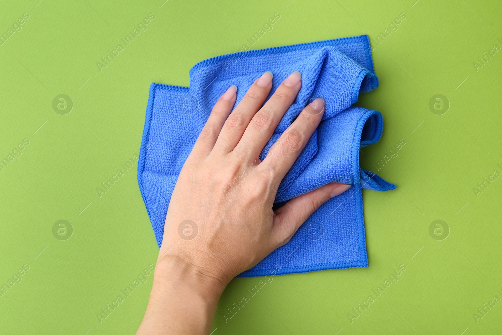 Photo of Woman with clean blue microfiber cloth on green background, top view