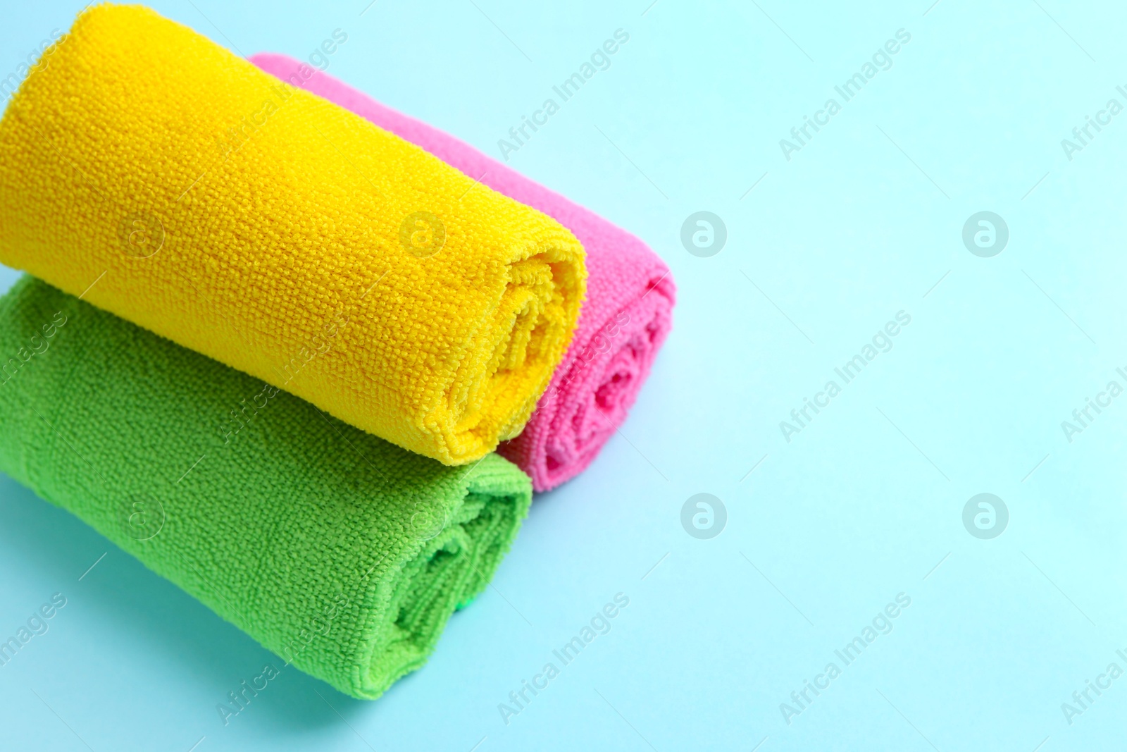 Photo of Rolled different microfiber cloths on light blue background, closeup. Space for text