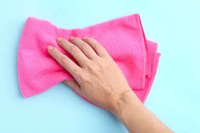 Photo of Woman with clean pink microfiber cloth on light blue background, top view