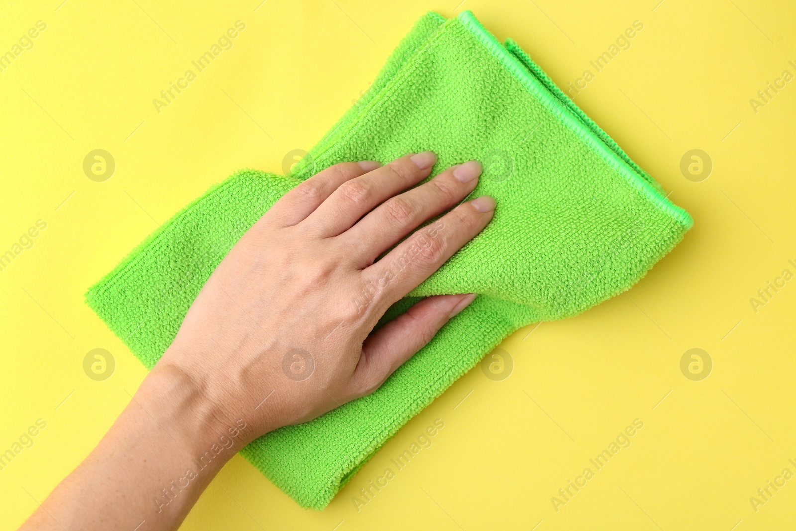 Photo of Woman with clean green microfiber cloth on yellow background, top view