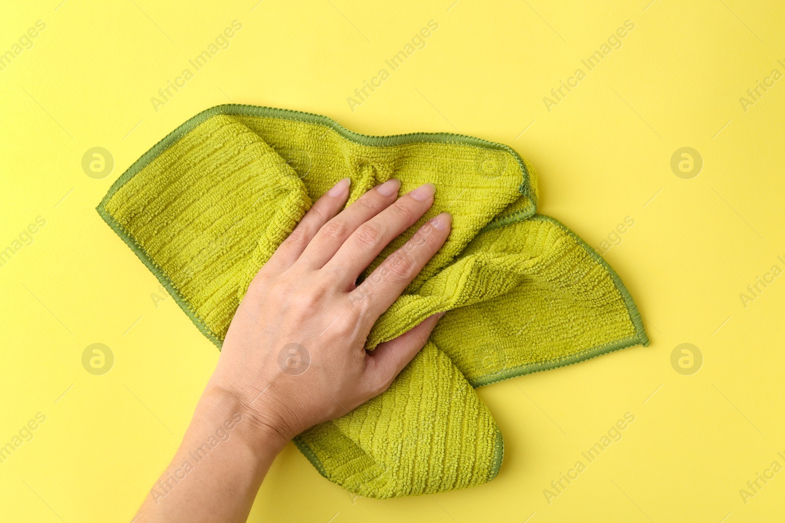 Photo of Woman with clean green microfiber cloth on yellow background, top view