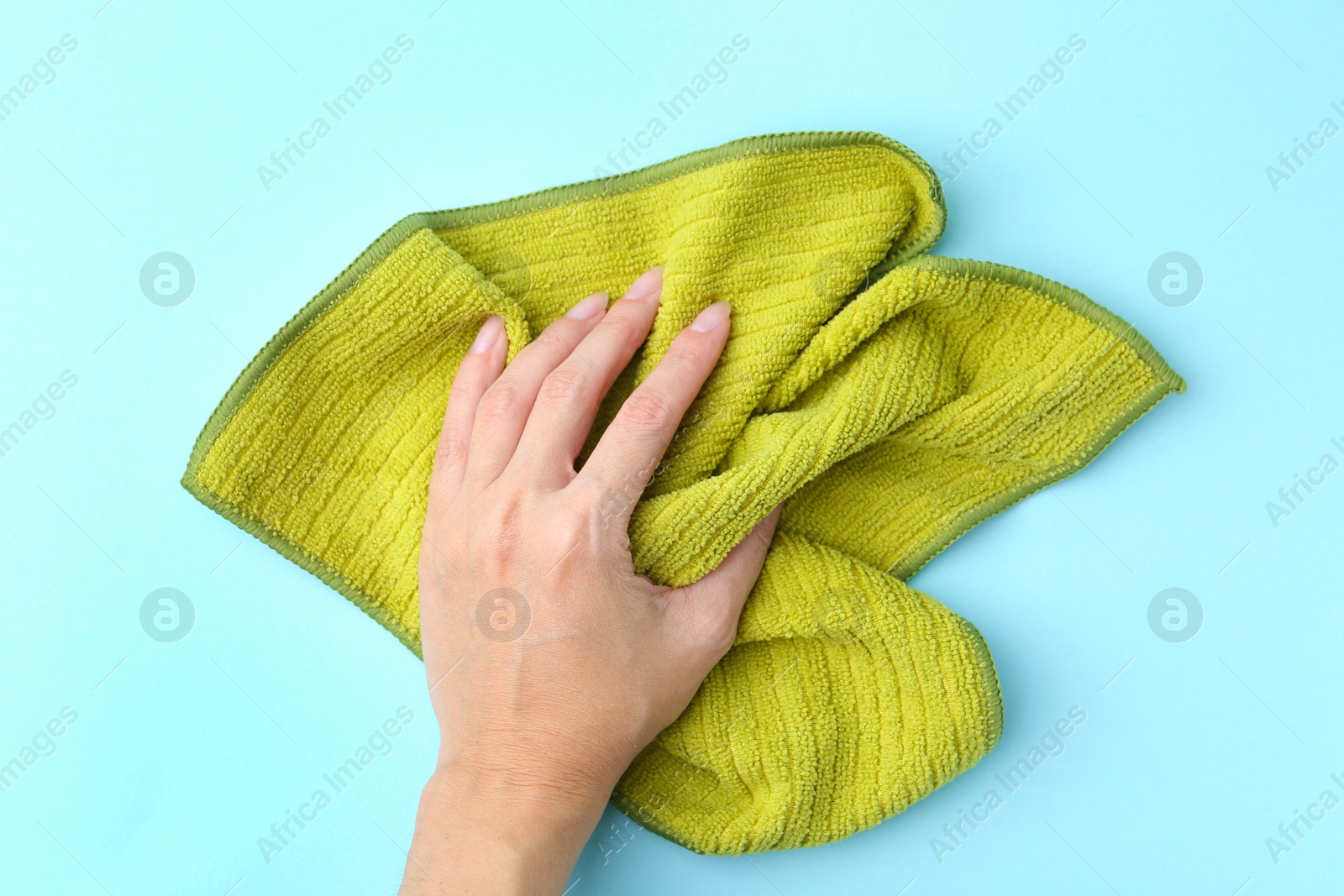 Photo of Woman with clean green microfiber cloth on light blue background, top view