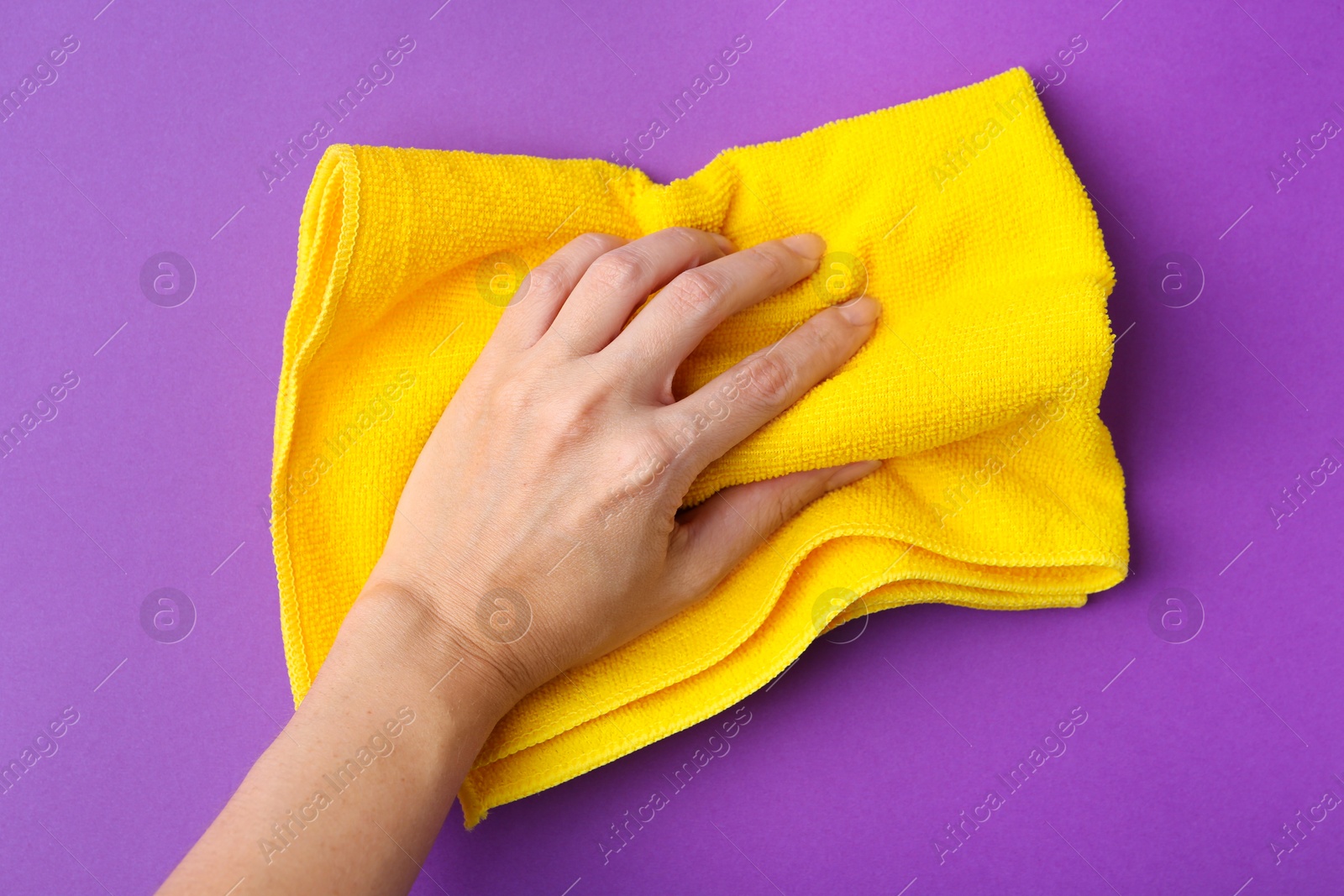 Photo of Woman with clean yellow microfiber cloth on purple background, top view