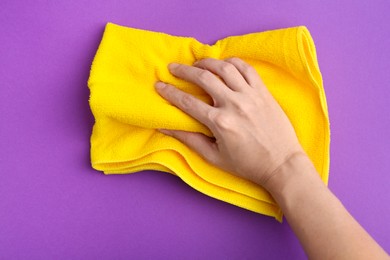 Photo of Woman with clean yellow microfiber cloth on purple background, top view