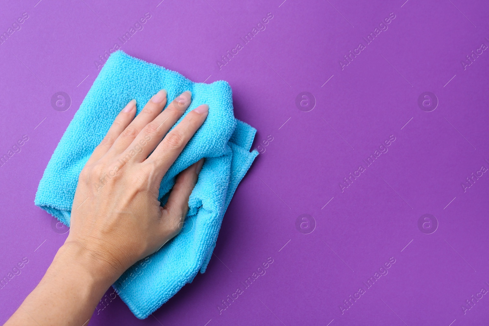 Photo of Woman with clean light blue microfiber cloth on purple background, top view. Space for text