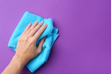 Photo of Woman with clean light blue microfiber cloth on purple background, top view. Space for text