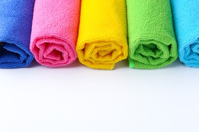 Photo of Rolled different microfiber cloths on white background, closeup. Space for text