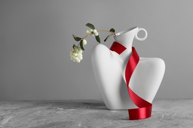 Photo of Stylish vase with snowberry branch and red ribbon on grey table, space for text