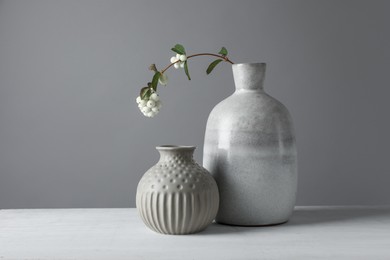 Photo of Stylish vases and snowberry branch on white table