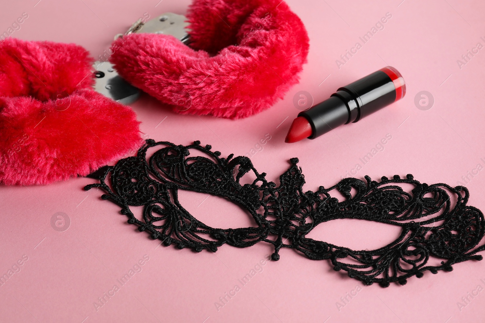 Photo of Fluffy handcuffs, lace mask and lipstick on pink background, closeup