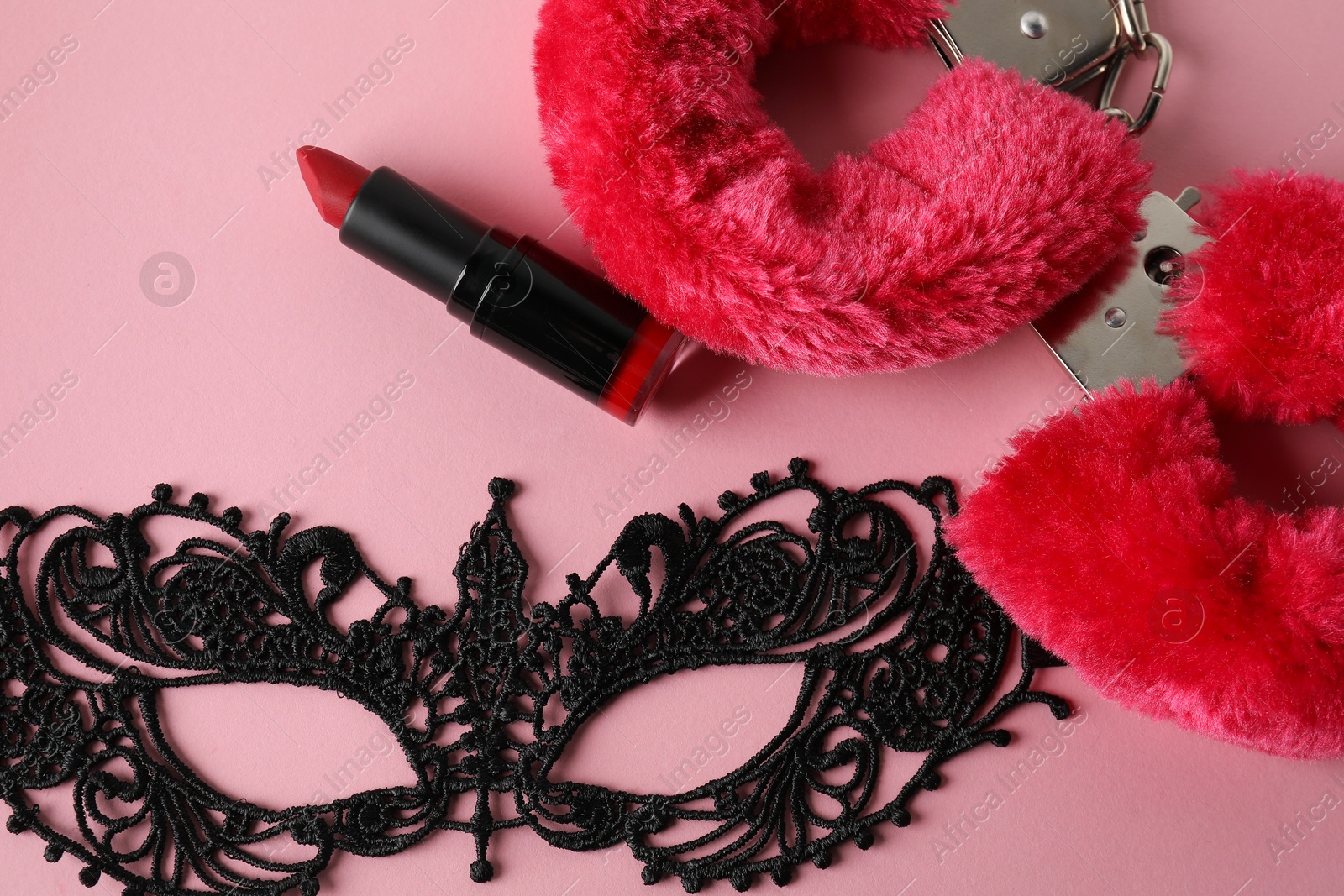 Photo of Fluffy handcuffs, lace mask and lipstick on pink background, flat lay