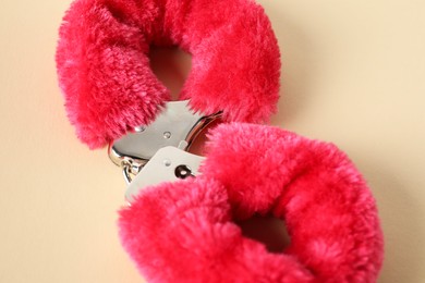 Photo of Pink fluffy handcuffs on pale yellow background, top view. Sex toy