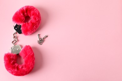 Photo of Fluffy handcuffs and keys on pink background, flat lay. Space for text