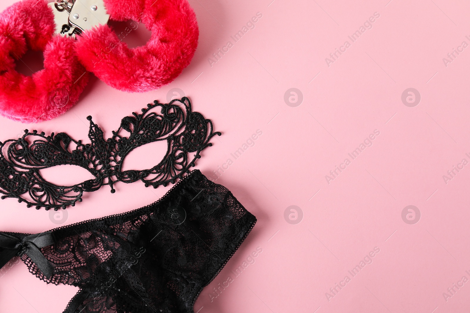 Photo of Fluffy handcuffs, lace mask and panties on pink background, flat lay. Space for text