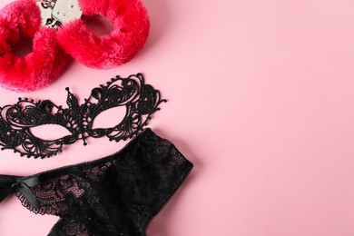 Photo of Fluffy handcuffs, lace mask and panties on pink background, flat lay. Space for text