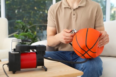 Photo of Man inflating basketball ball with air compressor indoors, closeup