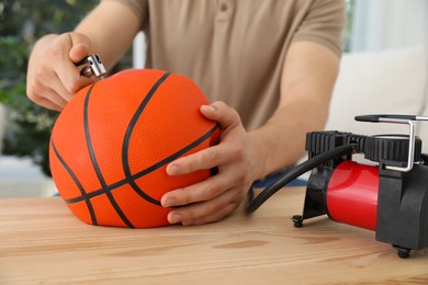 Photo of Man inflating basketball ball with air compressor indoors, closeup