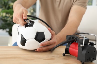 Photo of Man inflating soccer ball with air compressor indoors, closeup