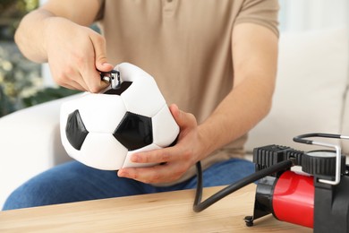 Photo of Man inflating soccer ball with air compressor indoors, closeup