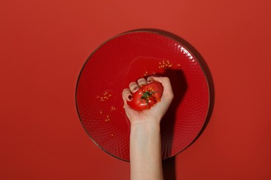 Photo of Woman smashing tomato on red background, top view