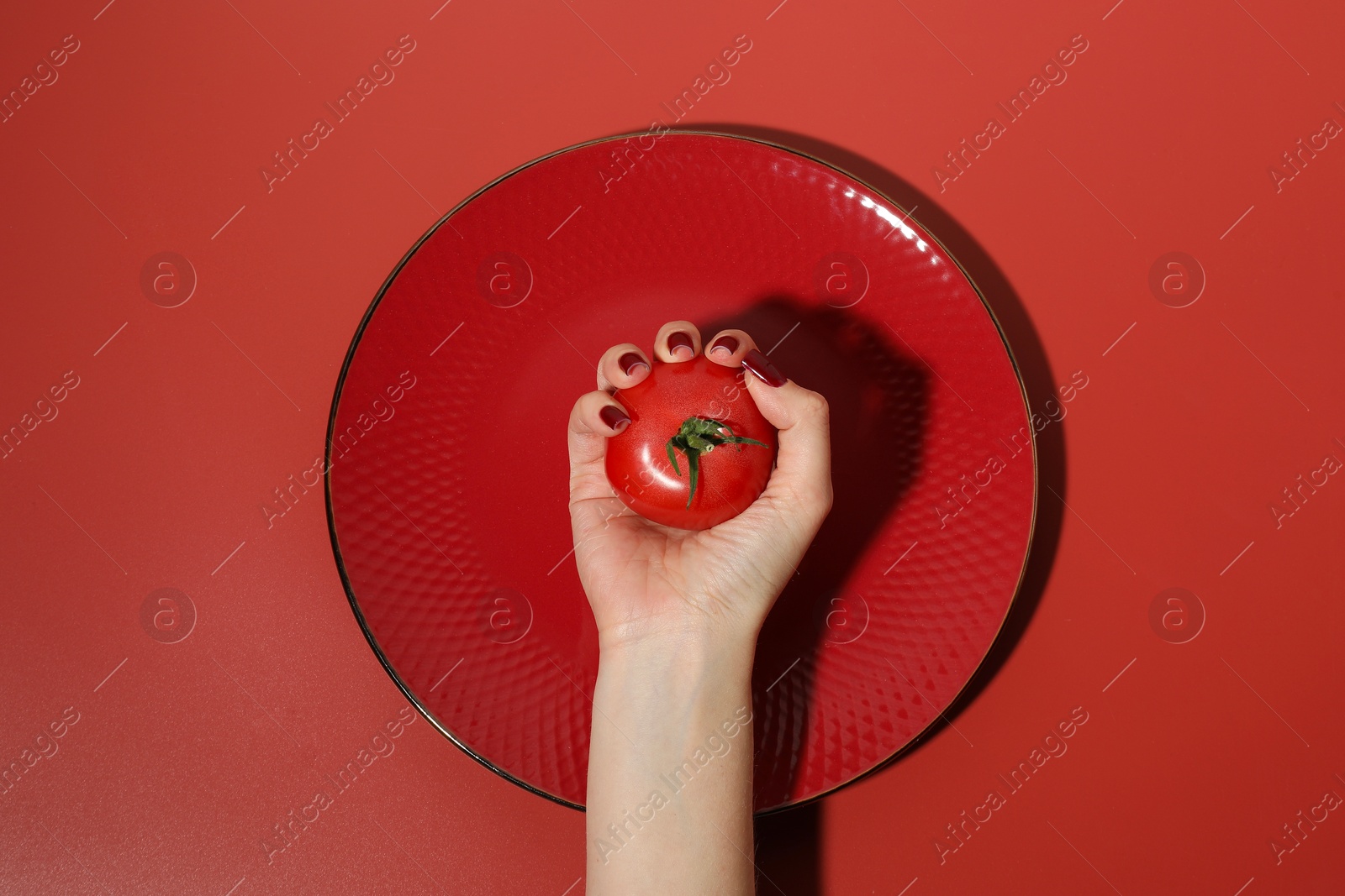 Photo of Woman holding tomato on red background, top view