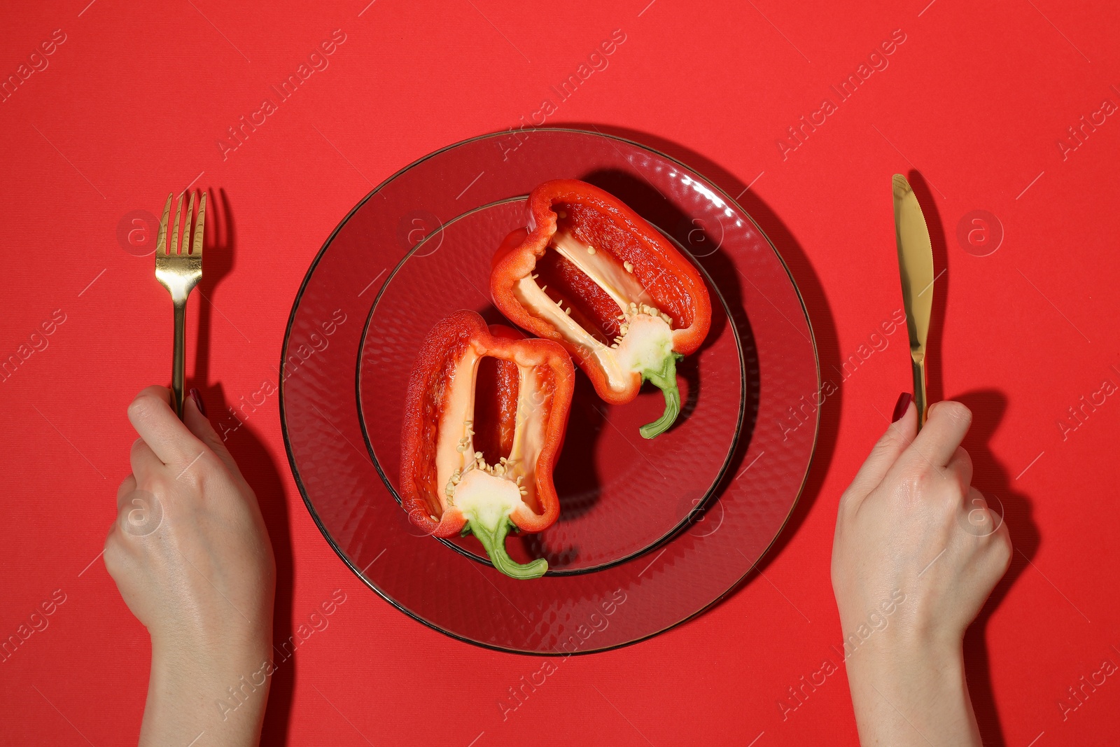 Photo of Woman with cutlery and halves of bell pepper on red background, top view