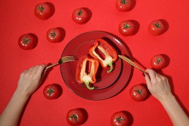 Photo of Woman eating bell pepper and tomatoes on red background, top view