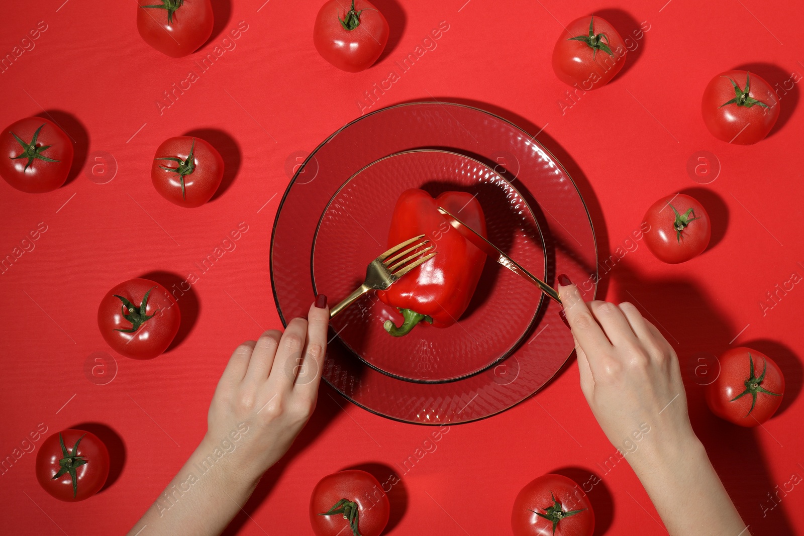 Photo of Woman eating bell pepper and tomatoes on red background, top view