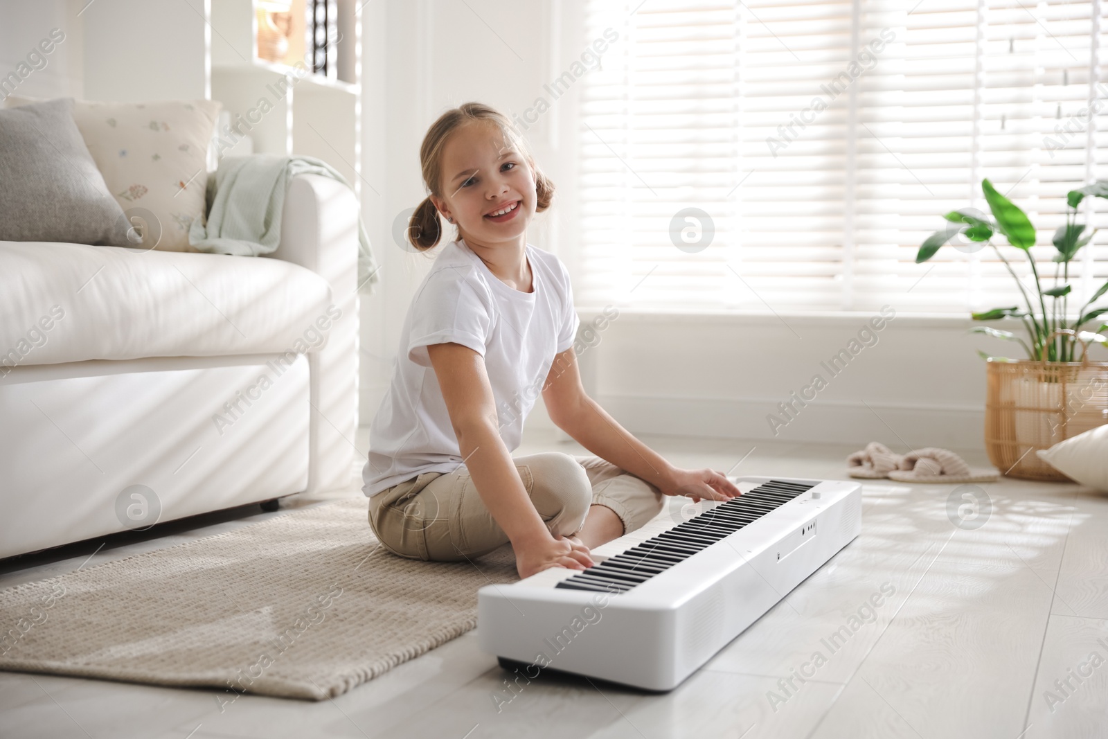 Photo of Cute girl playing synthesizer on floor at home