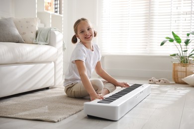 Cute girl playing synthesizer on floor at home