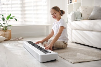 Cute girl playing synthesizer on floor at home