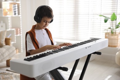 Photo of Cute boy in headphones playing synthesizer at home