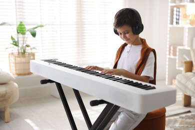 Photo of Cute boy in headphones playing synthesizer at home