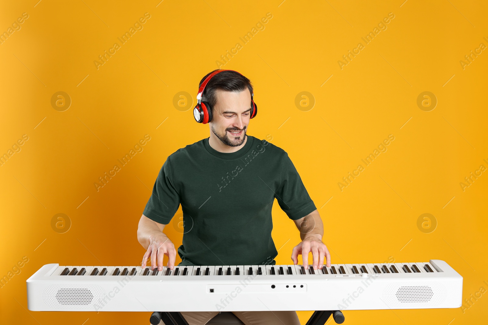 Photo of Smiling man in headphones playing synthesizer on orange background